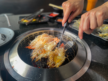 Crop nameless man with fork and knife consuming shrimps grilled in grill sizzling pot