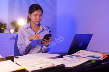 An Asian woman is working past common time at her desk inside the dwelling of job,busy viewing paperwork  her pocket book