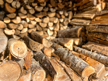 Neatly and randomly stacked hardwood firewood in a shed in preparation for winter heating season