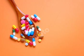 A vibrant sequence of tablets and nutritional vitamins on a wood spoon in opposition to an orange background