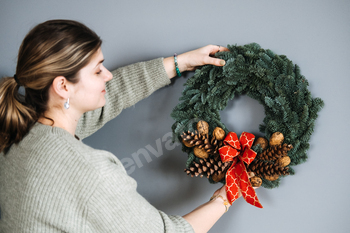 Girl placing a sustainable Christmas wreath fabricated from pure gives, that includes pinecones and a